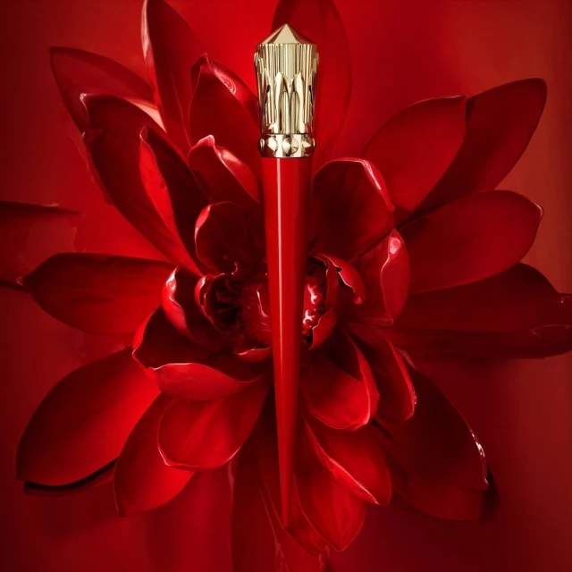Close-up studio shot of a red lipstick tube with a gold top, centered in front of a bright red flower-like background.