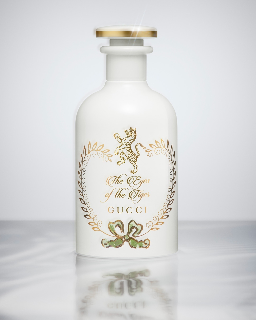 Product shot of a white perfume bottle by Gucci, decorated with gold details including a tiger, placed on a reflective marble surface.