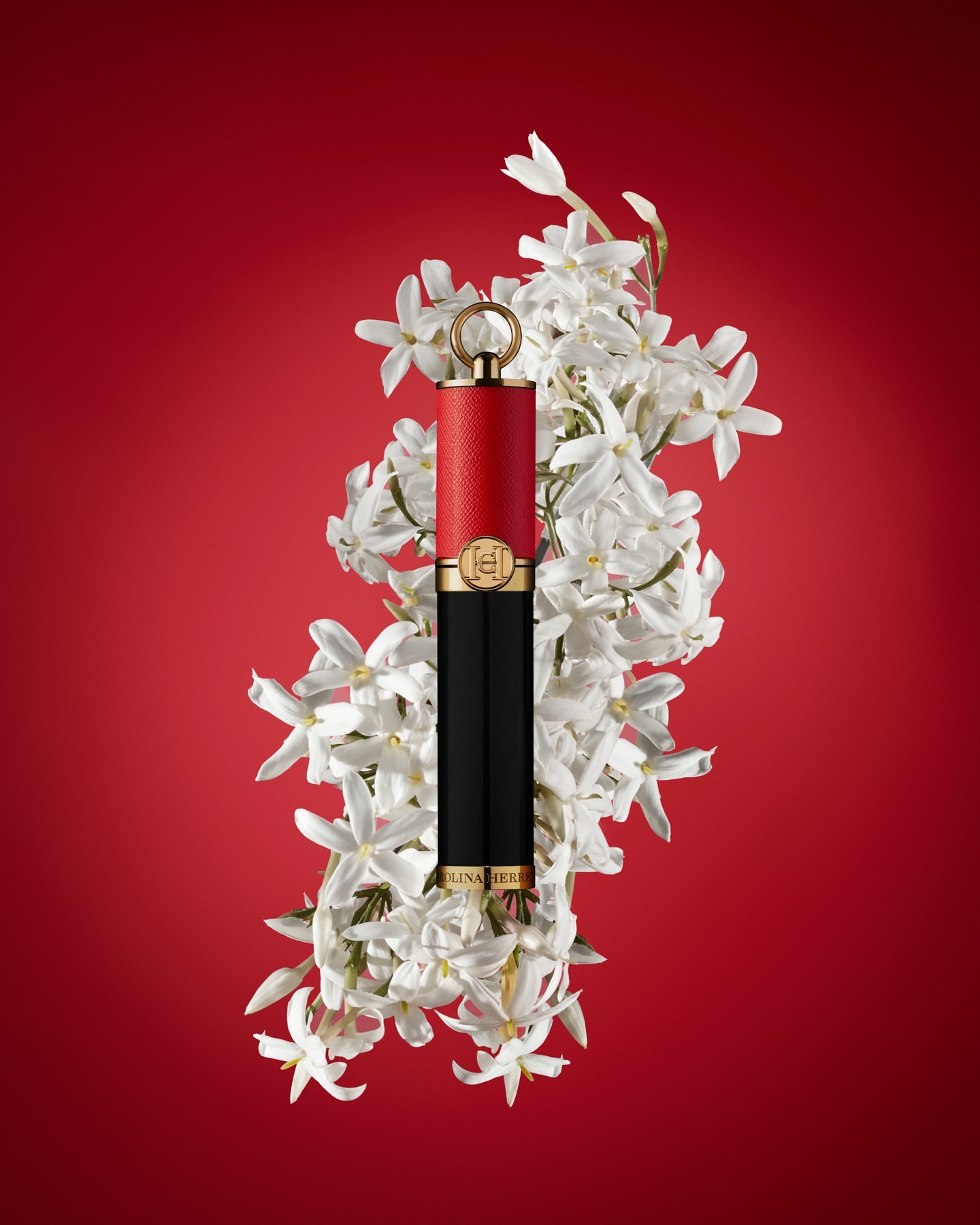 Carolina Herrera lipstick with white floral accents against a vibrant red background in a beauty and fashion editorial shot.