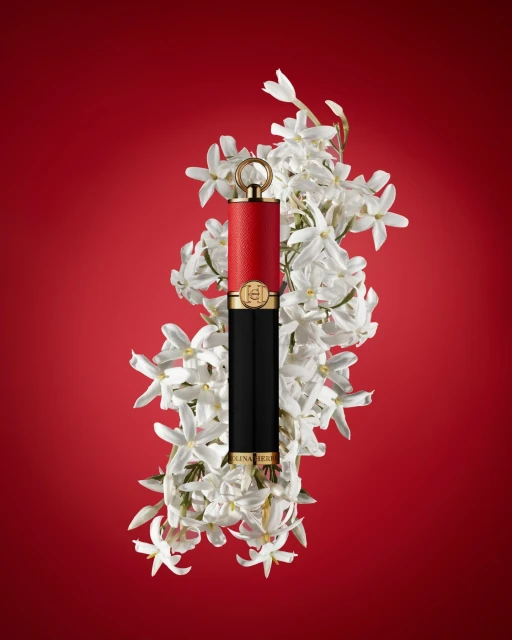 Carolina Herrera lipstick with white floral accents against a vibrant red background in a beauty and fashion editorial shot.