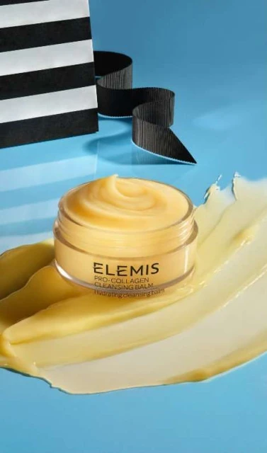 Cosmetic product jar of Elemis Pro-Collagen Cleansing Balm on pale yellow cream, with a Sephora shopping bag in the background.