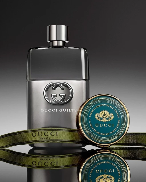 Gucci Guilty perfume bottle on a reflective surface with a Gucci beauty compact, set against a gradient gray backdrop in a studio setting.