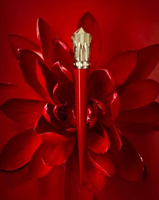 Red lipstick tube with a gold decorative top, set against a background of deep red flower petals, creating a luxurious beauty product shot.