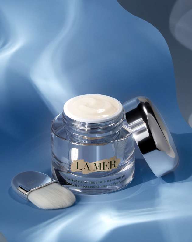 La Mer cream jar with applicator brush, set against a blue background, product shot for beauty and skincare advertising visuals.
