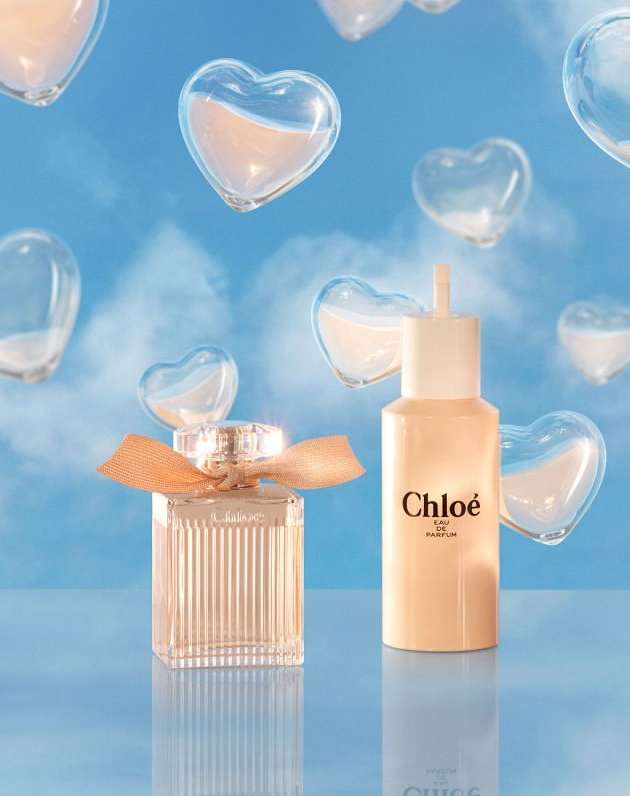 Two Chloe perfume bottles with peach ribbon against light blue sky with floating glass hearts in a beauty and fashion product shot.