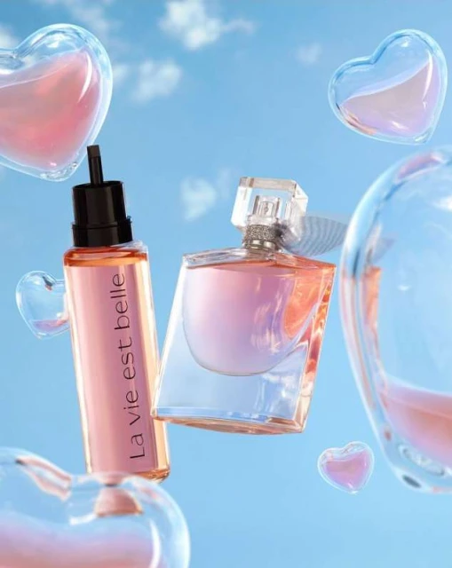 Two perfume bottles, with a transparent bottle of body oil, float in a blue sky with heart-shaped glass bubbles around them.