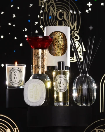 Luxury candles and fragrance products on a black platform against a dark backdrop featuring gold and white graphic accents, studio lighting.
