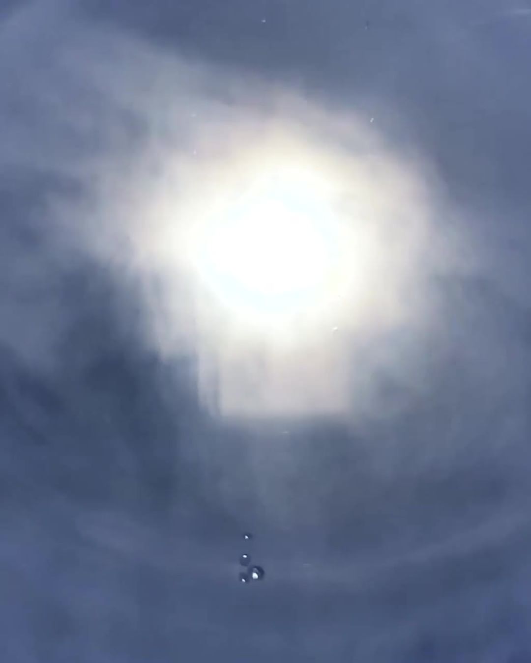 An abstract view of the sun with dark clouds and a few raindrops, creating a dreamy, atmospheric effect. The light is bright and diffused.