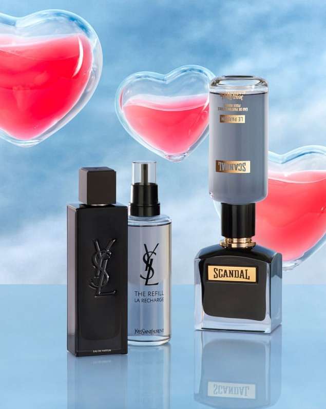 Close-up shot of Yves Saint Laurent and Scandal perfume bottles with heart-shaped transparent decor against a light blue background.