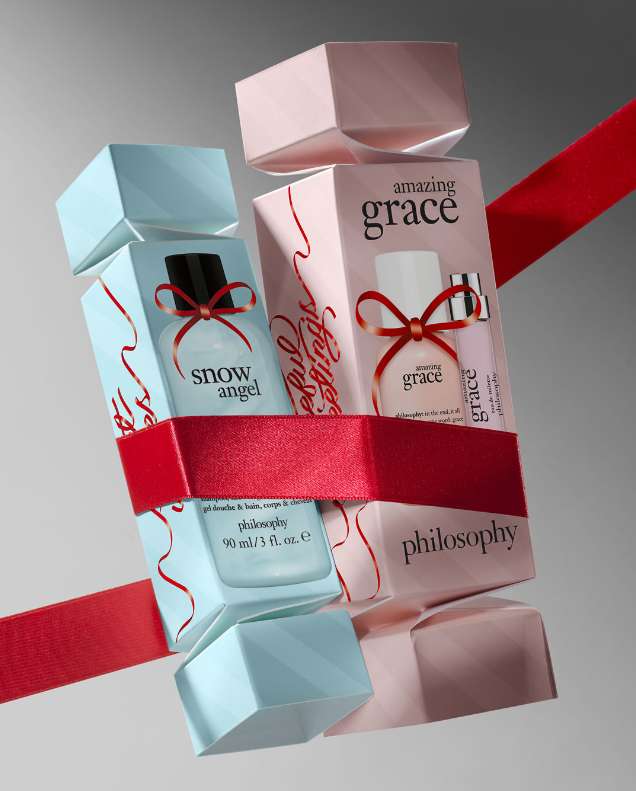 Stacked 'philosophy' brand fragrance gift sets wrapped with red ribbon. The fragrances include 'amazing grace' and 'snow angel'.