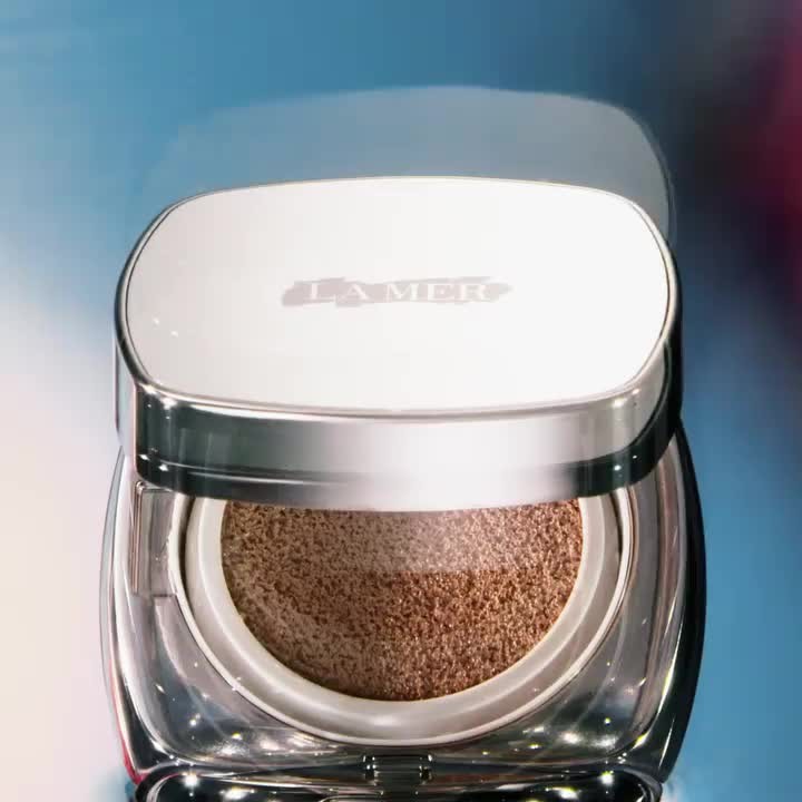 La Mer skincare product in a white and silver container. Product shot with a blurred blue and pink background.