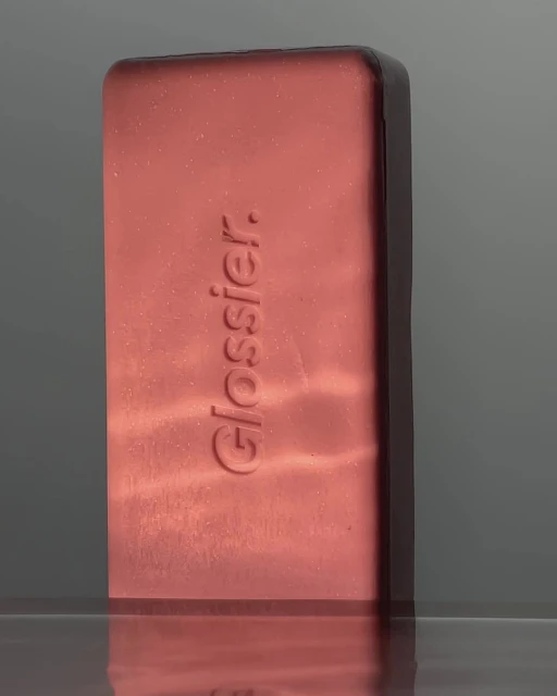 Close-up of Glossier bronzer compact in sleek, minimalist packaging, reflecting light on a glossy surface, studio shot.