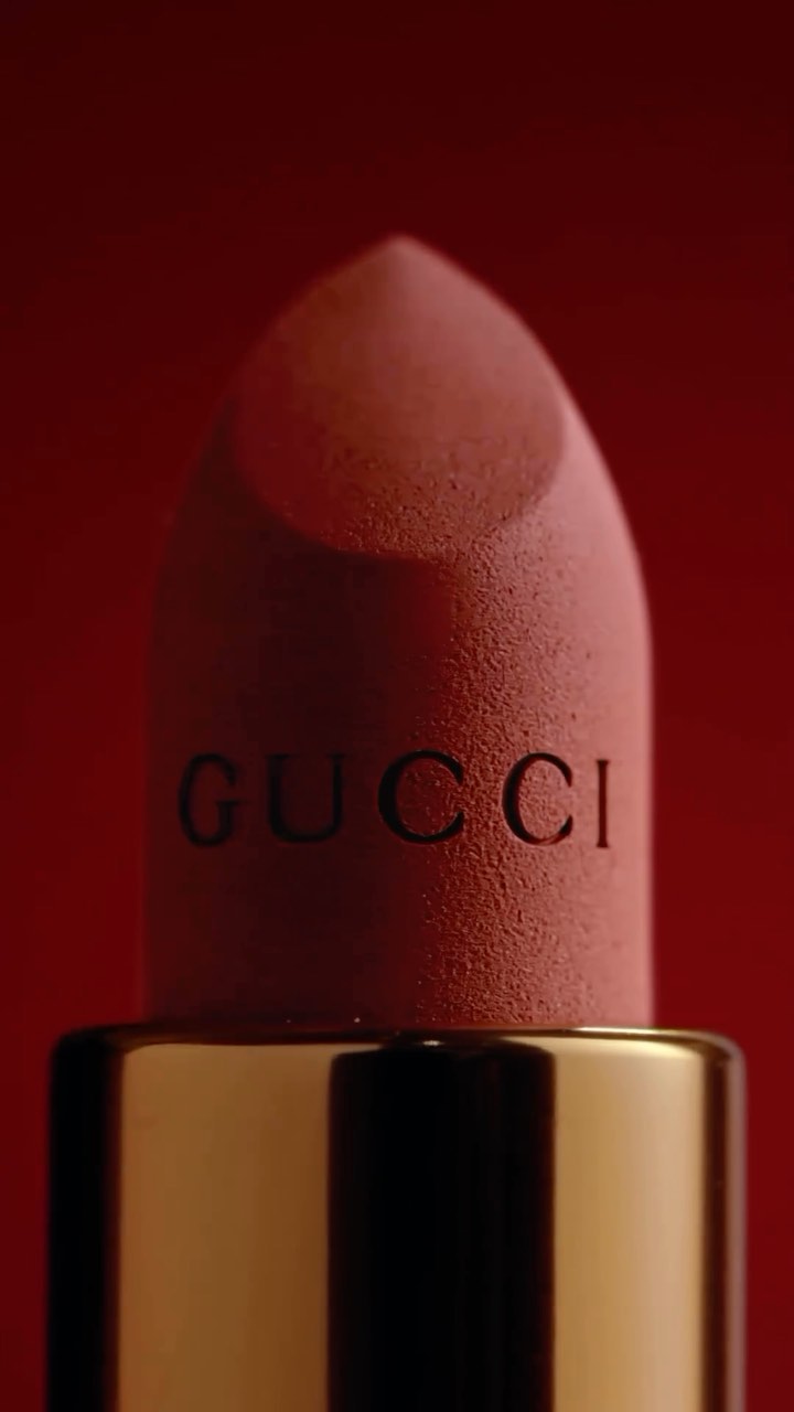 Macro studio shot of Gucci lipstick with a gold tube against a red background, perfect for beauty and fashion product presentation.