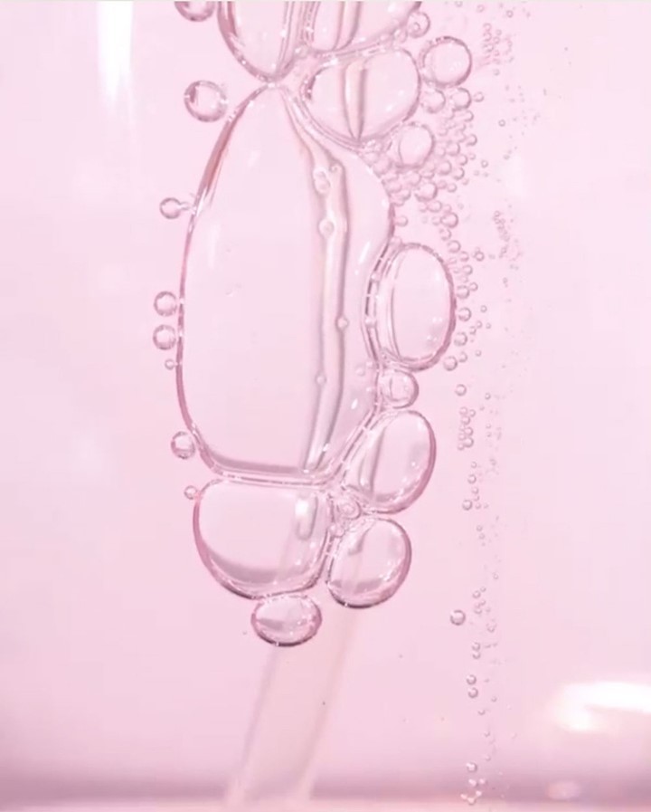 Close-up shot of transparent liquid with bubbles on a light pink background, creating a visually appealing and minimalist aesthetic.