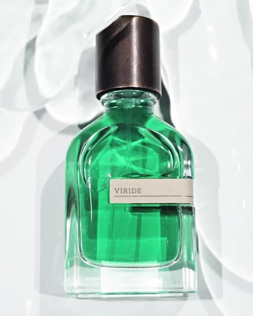 A green glass perfume bottle with a dark cap sits on a white surface with light reflecting, creating a clean and luxurious aesthetic.