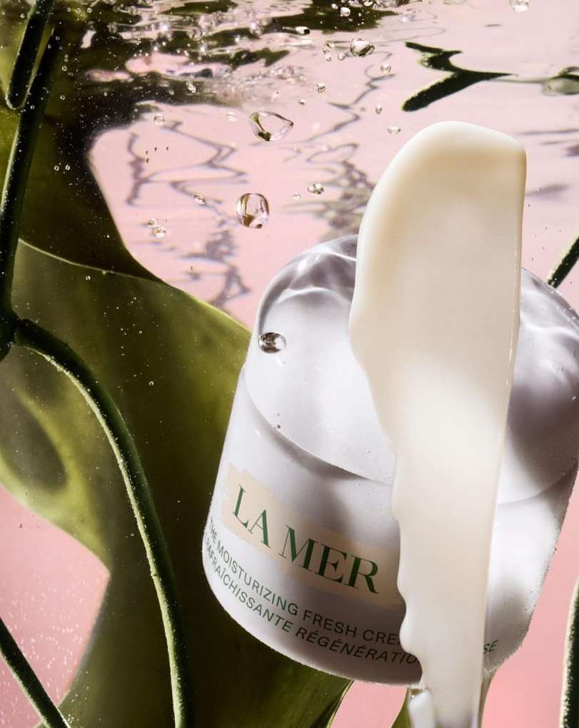 La Mer moisturizing cream product shot underwater with vibrant green foliage and water bubbles against a pink backdrop. Beauty.
