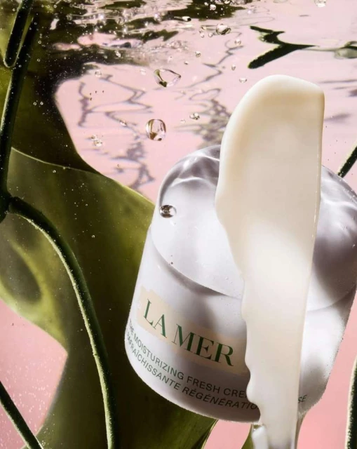 La Mer moisturizing cream product shot underwater with vibrant green foliage and water bubbles against a pink backdrop. Beauty.