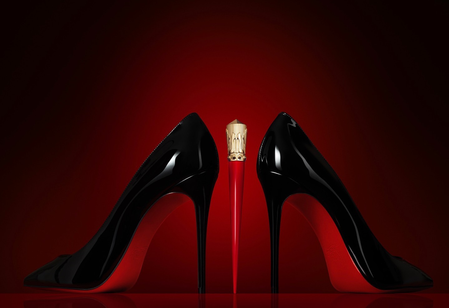 High-fashion product shot featuring black patent leather stiletto pumps and a red lipstick tube, presented on a matching red surface.