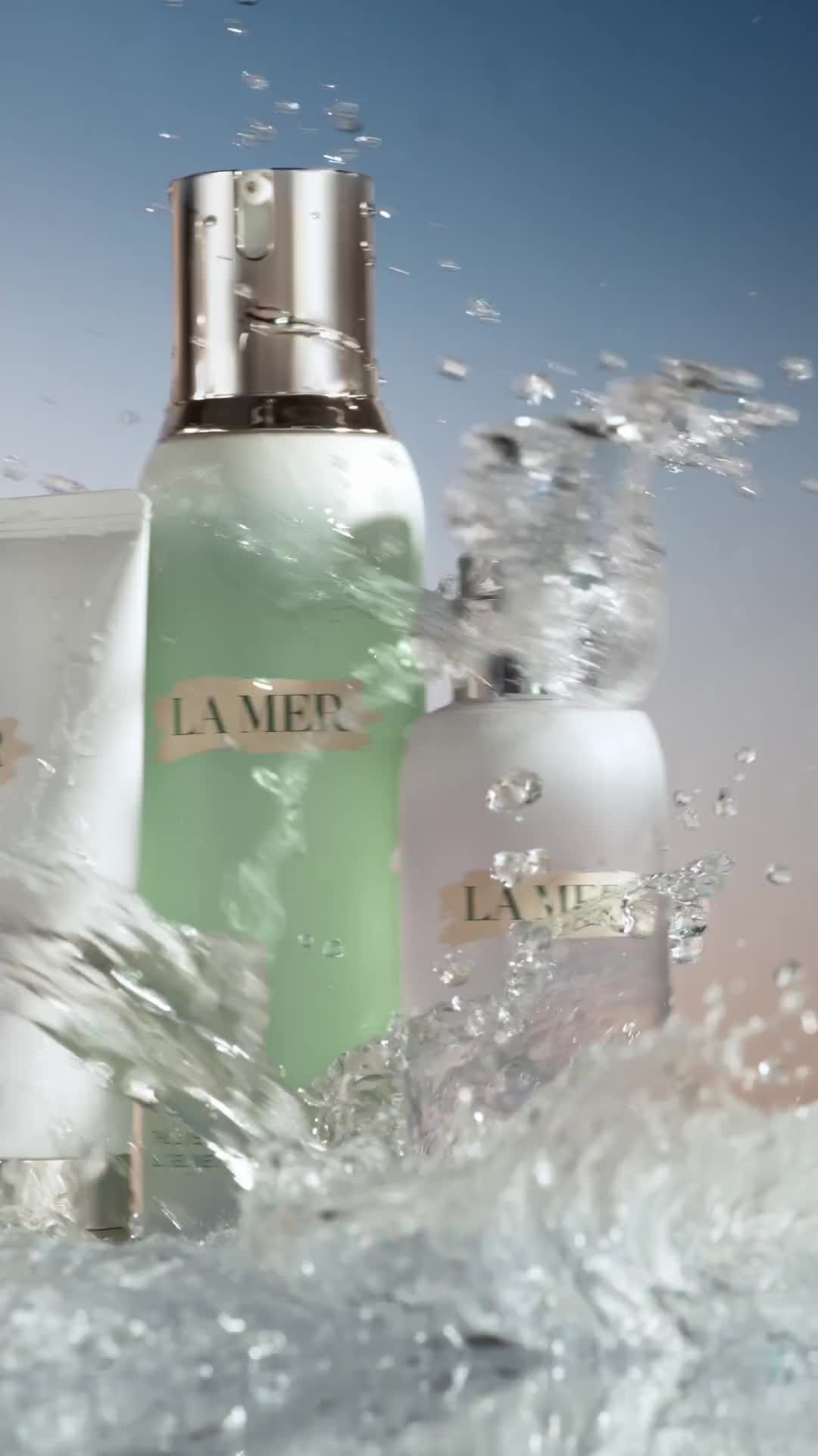 La Mer skin care products in a vertical studio shot with splashes of water in the foreground and a gradient blue background.