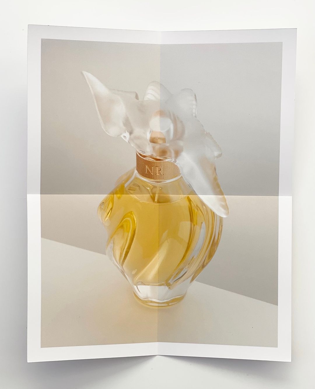 Still life shot of a perfume bottle on a white surface. The bottle has a clear, sculptural design and a translucent cap.