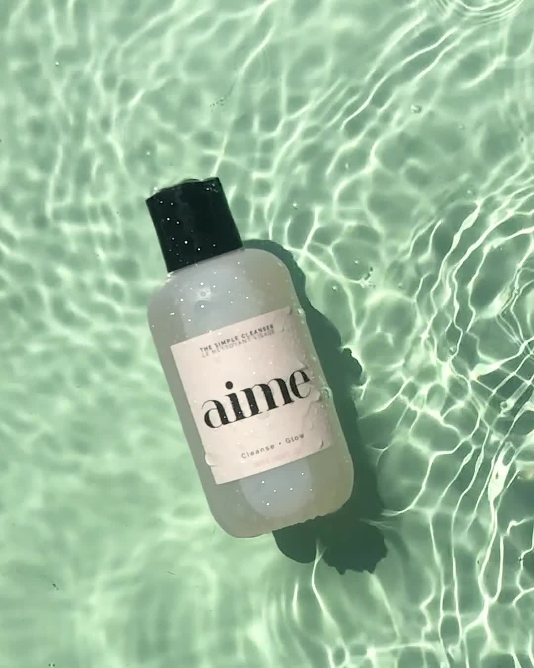 Cosmetic cleanser by Aime in clear bottle with green cap, floating in water with textured rippled surface and light green background.