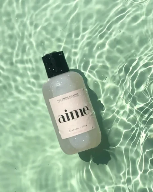Cosmetic cleanser by Aime in clear bottle with green cap, floating in water with textured rippled surface and light green background.