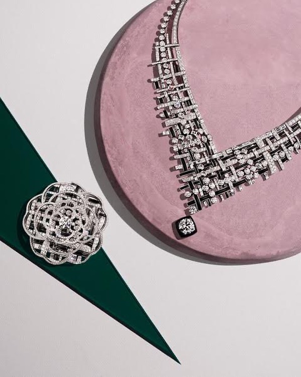 High-angle studio shot of a diamond necklace and flower brooch arranged on a pink and green surface, displaying luxury jewelry.