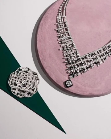High-angle studio shot of a diamond necklace and flower brooch arranged on a pink and green surface, displaying luxury jewelry.