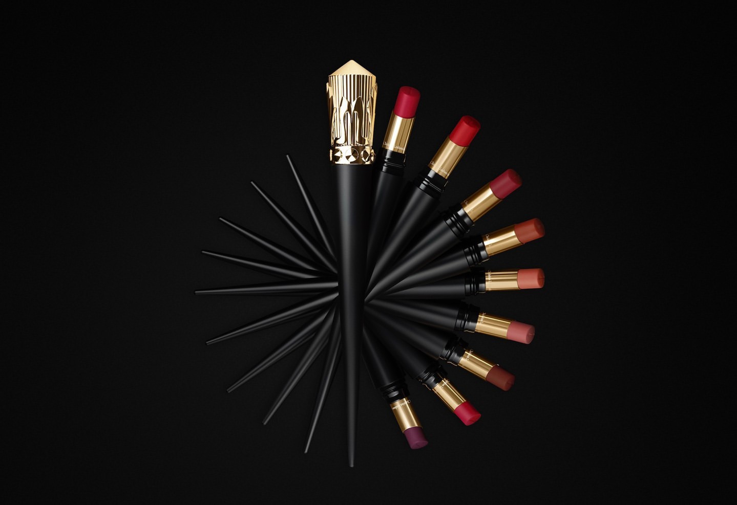 Elevated shot of black and gold lipsticks arranged in a semi-circular pattern against a solid black backdrop, showcasing the beauty product.