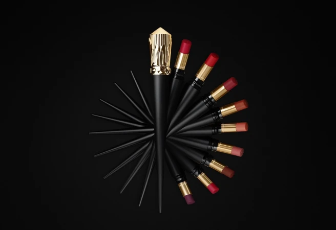 Elevated shot of black and gold lipsticks arranged in a semi-circular pattern against a solid black backdrop, showcasing the beauty product.