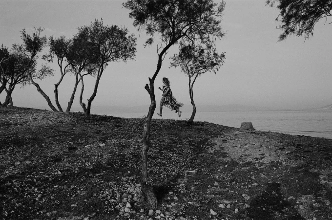 Black and white photograph of a woman running among sparse trees along a coastal slope by Vincent Van De Wijngaard.