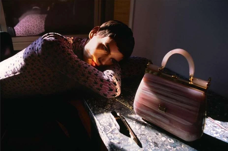 Adult laying head on arms with a handbag on a dark marble surface in a dimly lit interior setting.