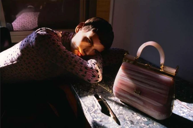 Adult laying head on arms with a handbag on a dark marble surface in a dimly lit interior setting.