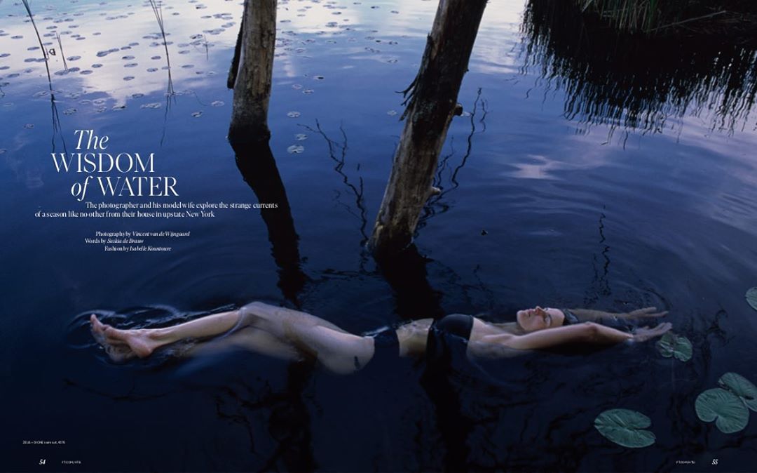 Woman floats in dark water between tree trunks and lily pads under dim light in a cinematic, editorial, fashion, and nature photograph.