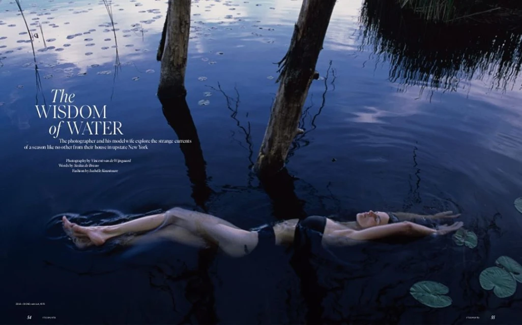 Woman floats in dark water between tree trunks and lily pads under dim light in a cinematic, editorial, fashion, and nature photograph.