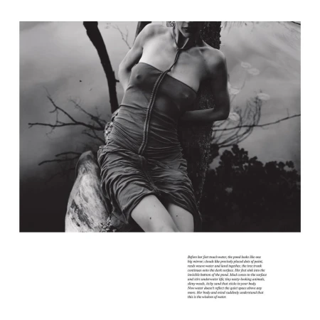 Monochrome portrait of a woman in a draped dress, partially submerged in water, leaning against a tree near a pond, in a fine art style.