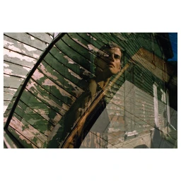 Reflective double exposure portrait of a man looking upward against a weathered wooden building exterior