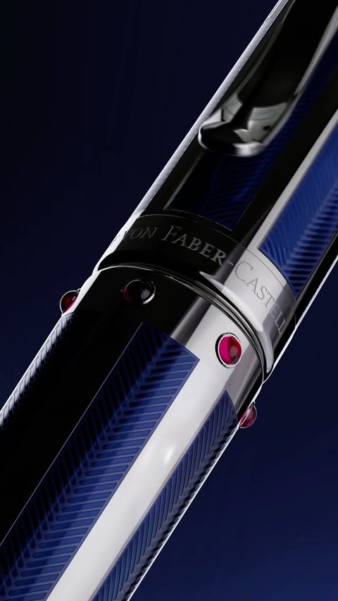 Close-up of a luxury writing pen featuring a silver body, blue detailing, embedded red jewels, and visible text branding on a dark blue background.