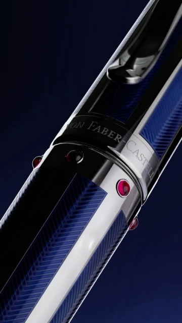 Close-up of a luxury writing pen featuring a silver body, blue detailing, embedded red jewels, and visible text branding on a dark blue background.