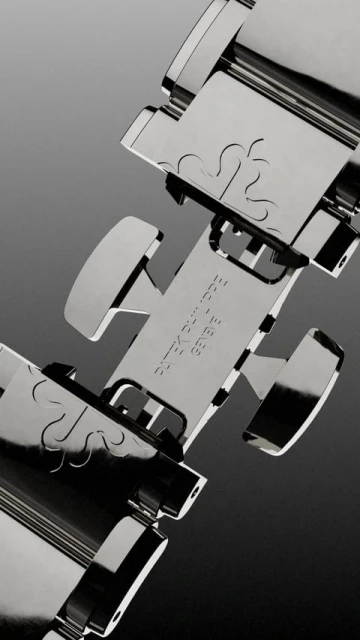 Close-up studio shot of a shiny metal Patek Philippe watch bracelet featuring a deployment clasp with engraved details on a grey gradient background.