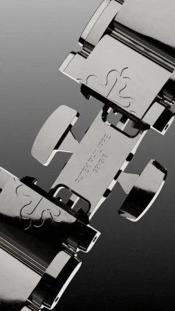 Close-up studio shot of a shiny metal Patek Philippe watch bracelet featuring a deployment clasp with engraved details on a grey gradient background.