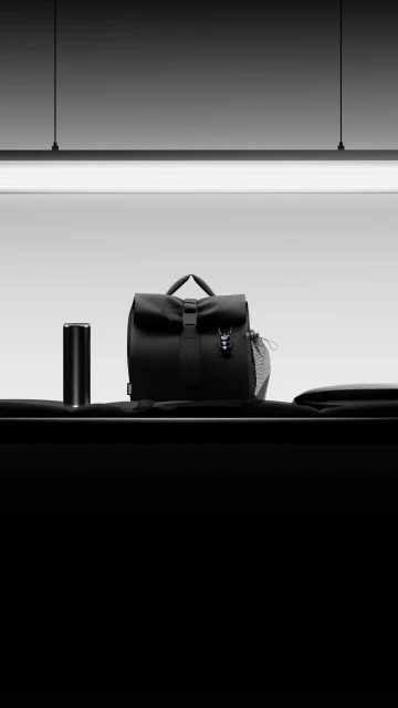 Black backpack and thermos sit on a table in a studio with black and white colors, minimalist composition, and sleek design.