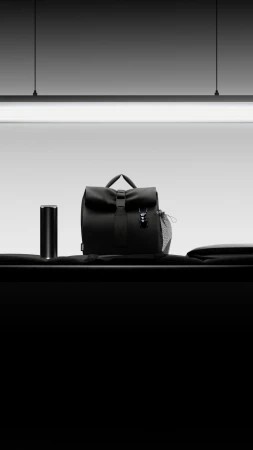 Black backpack and thermos sit on a table in a studio with black and white colors, minimalist composition, and sleek design.