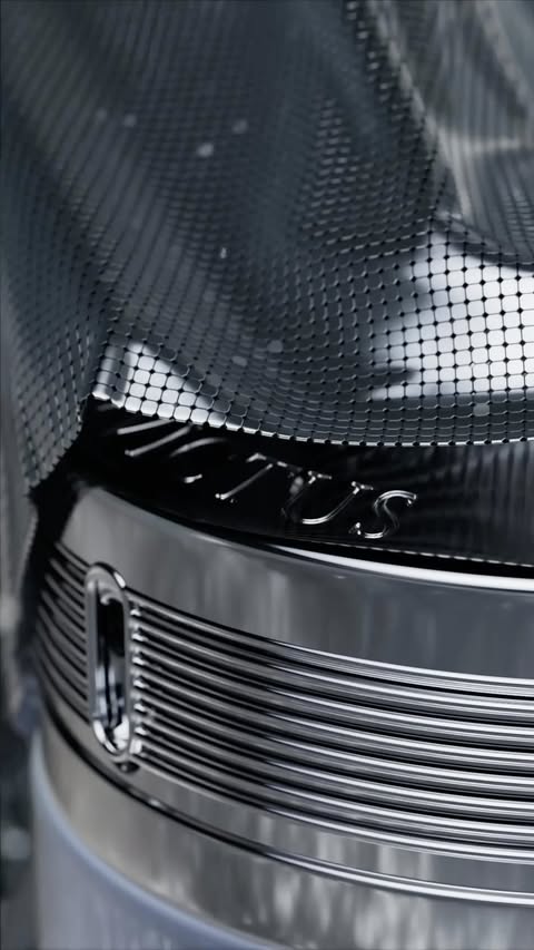 Close-up of shiny metal object with mesh netting and engraved logo, showcasing industrial design with a focus on texture and detail.