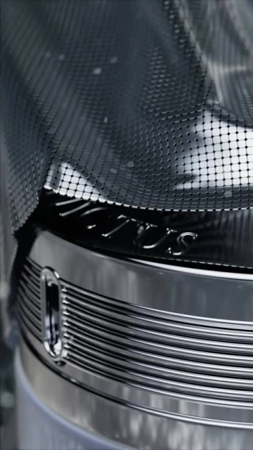 Close-up of shiny metal object with mesh netting and engraved logo, showcasing industrial design with a focus on texture and detail.