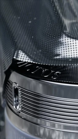 Close-up of shiny metal object with mesh netting and engraved logo, showcasing industrial design with a focus on texture and detail.