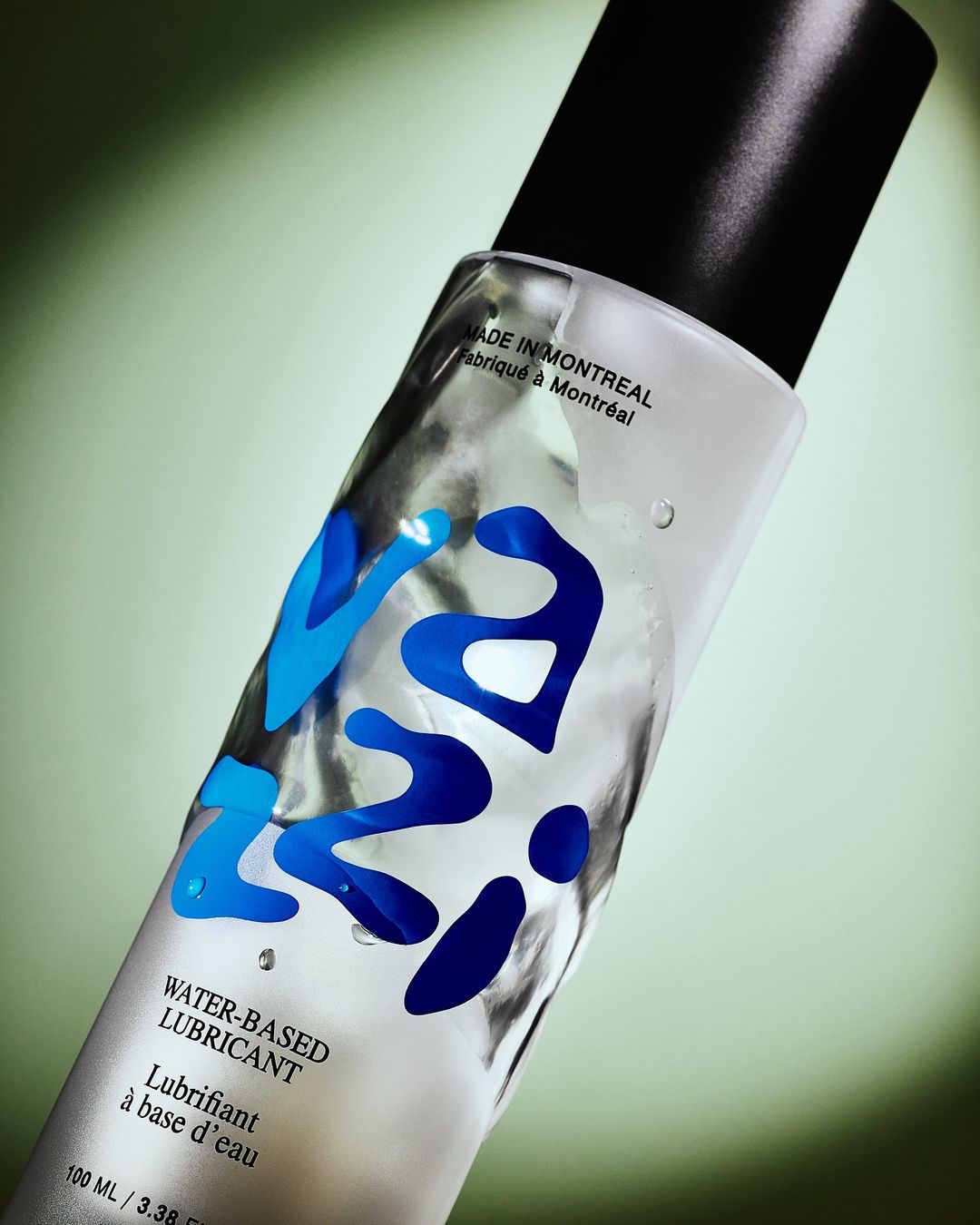 Clear bottle of water-based lubricant with blue lettering against a soft green background, product shot for beauty or healthcare.
