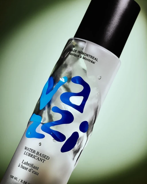 Clear bottle of water-based lubricant with blue lettering against a soft green background, product shot for beauty or healthcare.