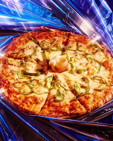 Overhead shot of a sliced pizza with green peppers and a bread roll in the center, resting on a metallic blue reflective surface.
