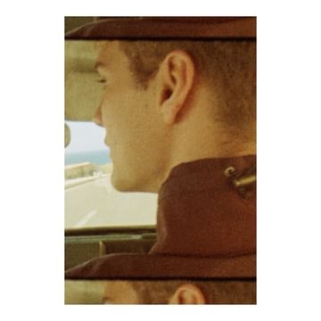 Profile shot of a man driving a car on a coastal road, showcasing his ear, neck, and the landscape visible through the window.